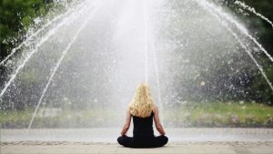Frau betreibt in Natur geführte Meditation MBSR (Mindfulness Based Stress Reduction). Ruhiges Bild mit Wasser und Bäumen