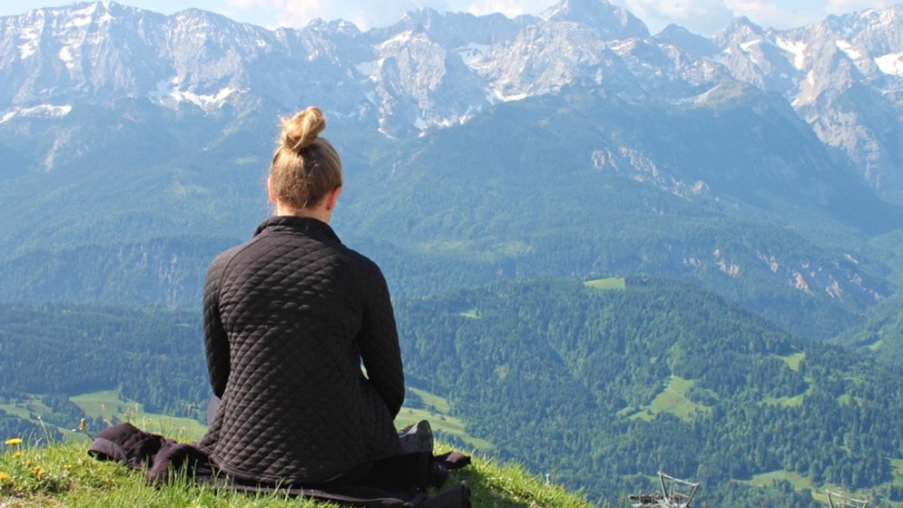 Frau sitzt in Natur und meditiert. Führt Meditationsübungen durch